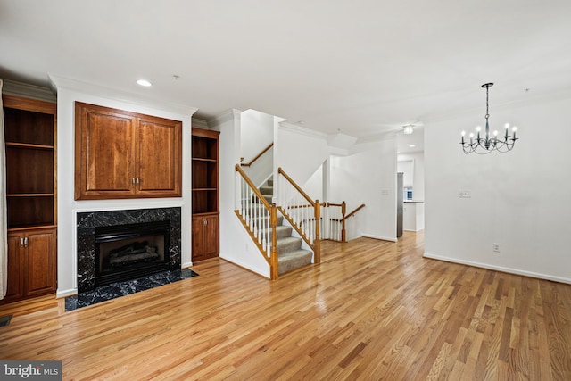 unfurnished living room with a notable chandelier, light wood-type flooring, crown molding, and a premium fireplace