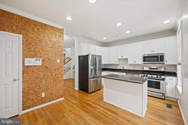 kitchen featuring light wood-type flooring, ornamental molding, stainless steel appliances, white cabinets, and a kitchen island