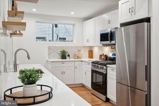 kitchen with appliances with stainless steel finishes, sink, light wood-type flooring, backsplash, and white cabinets