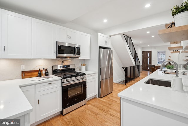 kitchen with tasteful backsplash, white cabinetry, sink, light hardwood / wood-style floors, and stainless steel appliances