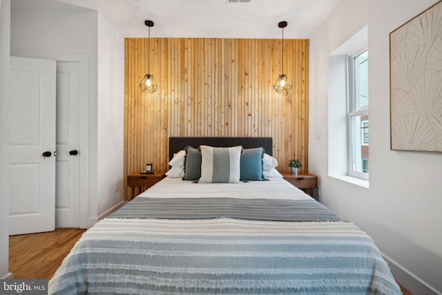 bedroom with multiple windows, wooden walls, and hardwood / wood-style floors