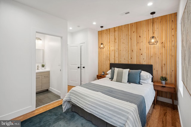 bedroom with wood walls, ensuite bath, and hardwood / wood-style flooring