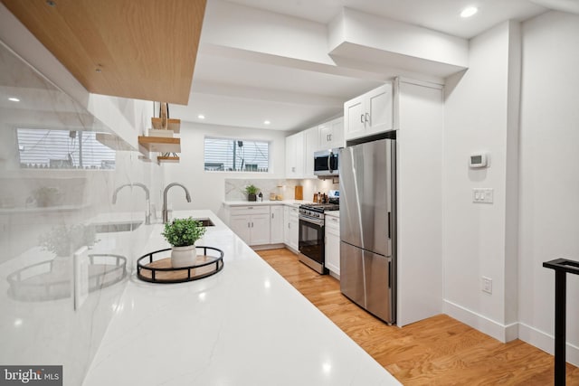 kitchen featuring appliances with stainless steel finishes, sink, light hardwood / wood-style floors, white cabinets, and decorative backsplash