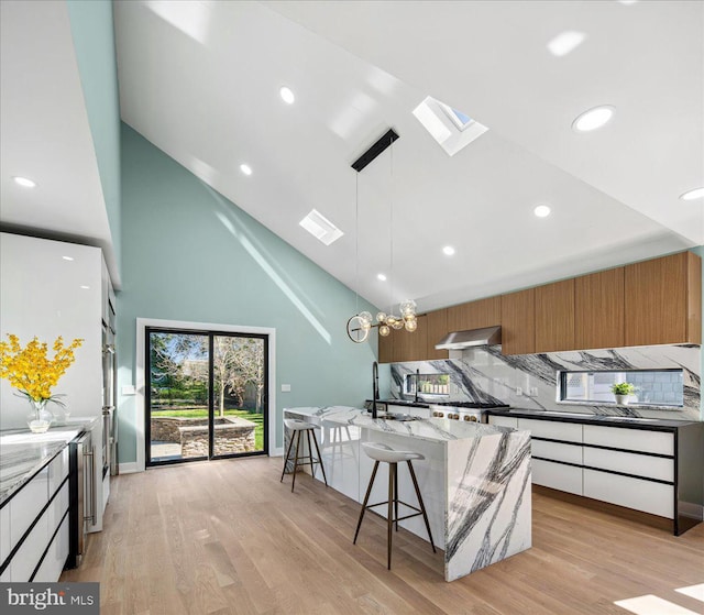 261 Moore St, Princeton, NJ 08540 - kitchen featuring a skylight, light stone counters, high vaulted ceiling, wall chimney exhaust hood, and modern cabinets