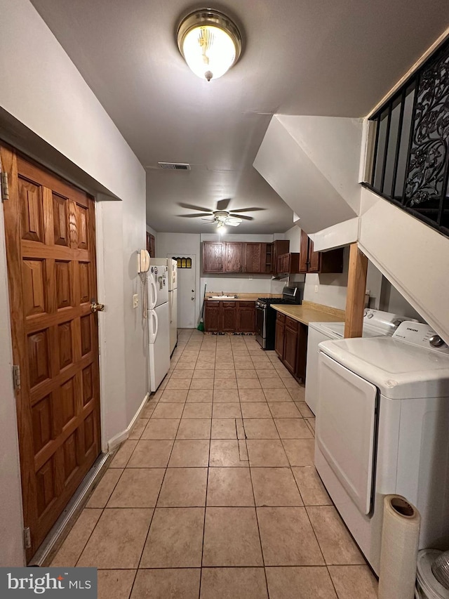 kitchen featuring ceiling fan, light tile patterned floors, separate washer and dryer, white fridge, and stainless steel range with gas cooktop