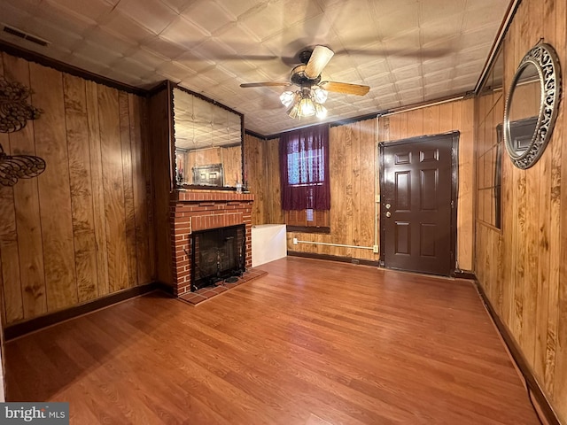 unfurnished living room with ceiling fan, hardwood / wood-style flooring, wooden walls, and a fireplace