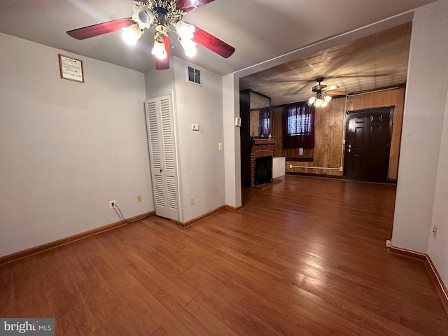 unfurnished living room with dark wood-type flooring, ceiling fan, and wooden walls