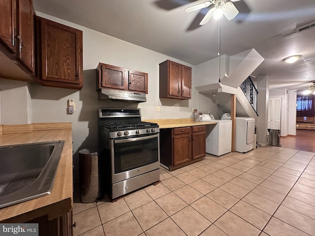 kitchen with stainless steel gas stove, light tile patterned flooring, washer and dryer, and ceiling fan