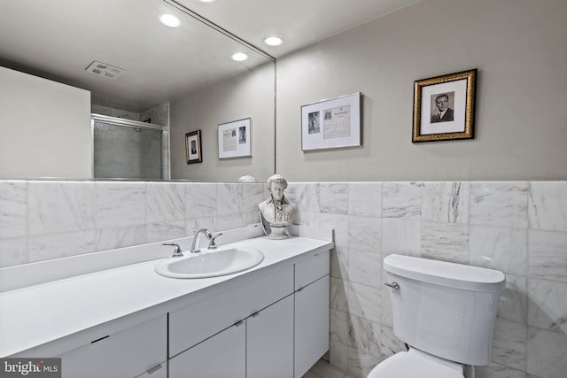 bathroom featuring a shower with shower door, vanity, toilet, and tile walls