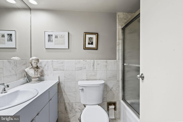 full bathroom with tile walls, shower / bath combination with glass door, toilet, and vanity