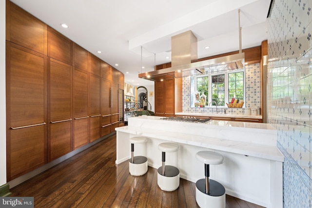 kitchen featuring stainless steel gas cooktop, hanging light fixtures, a kitchen breakfast bar, dark wood-type flooring, and light stone counters