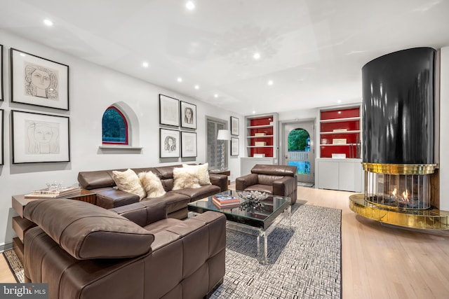 living room featuring a multi sided fireplace, built in shelves, and light hardwood / wood-style floors