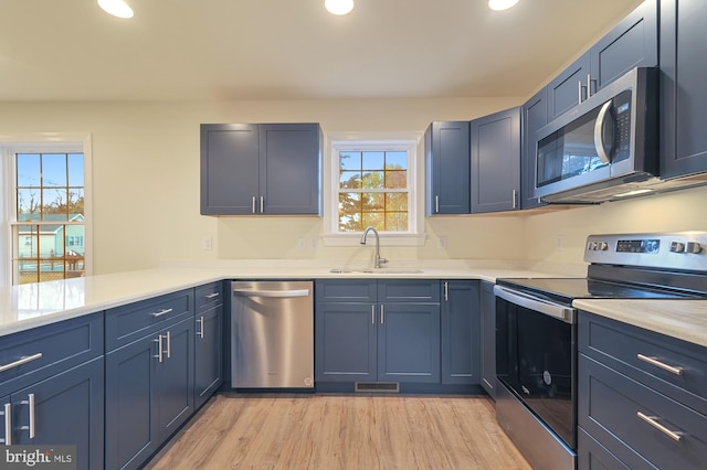 kitchen featuring blue cabinetry, appliances with stainless steel finishes, sink, and light hardwood / wood-style flooring