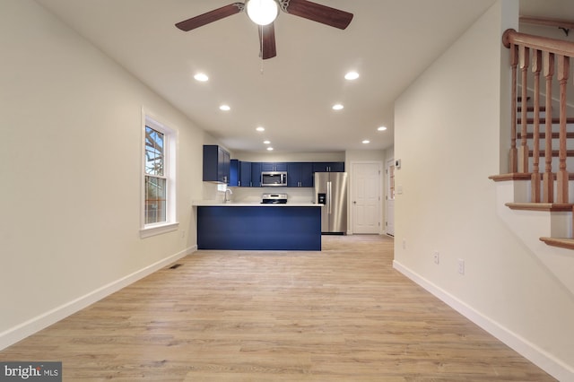 kitchen with appliances with stainless steel finishes, kitchen peninsula, a kitchen bar, blue cabinets, and light wood-type flooring