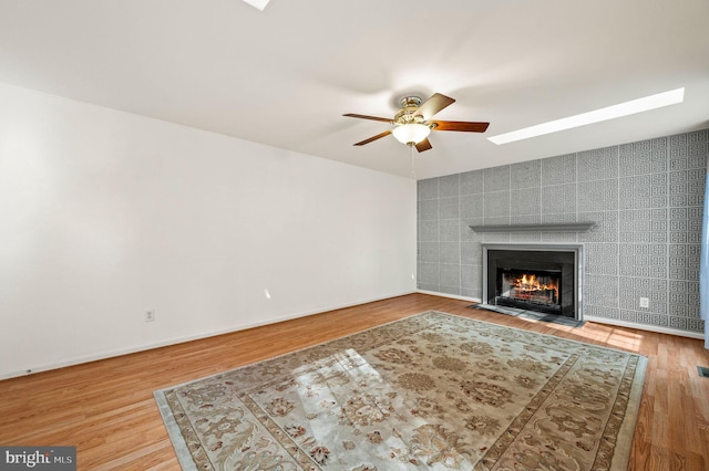 unfurnished living room featuring hardwood / wood-style flooring, tile walls, ceiling fan, and a tiled fireplace