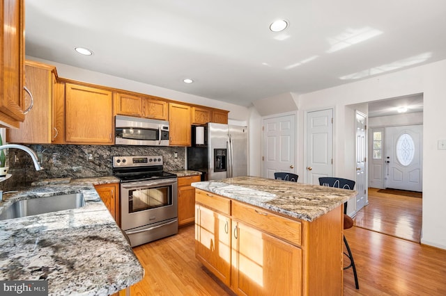 kitchen featuring sink, a center island, light stone counters, light hardwood / wood-style flooring, and appliances with stainless steel finishes