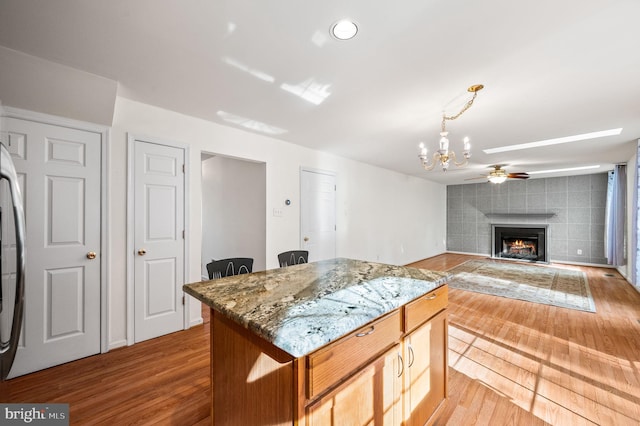 kitchen with light stone countertops, ceiling fan with notable chandelier, a fireplace, a center island, and light hardwood / wood-style floors