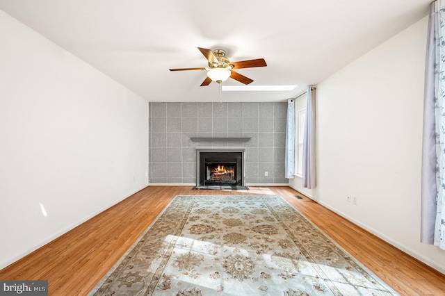 unfurnished living room with hardwood / wood-style floors, ceiling fan, tile walls, and a tiled fireplace