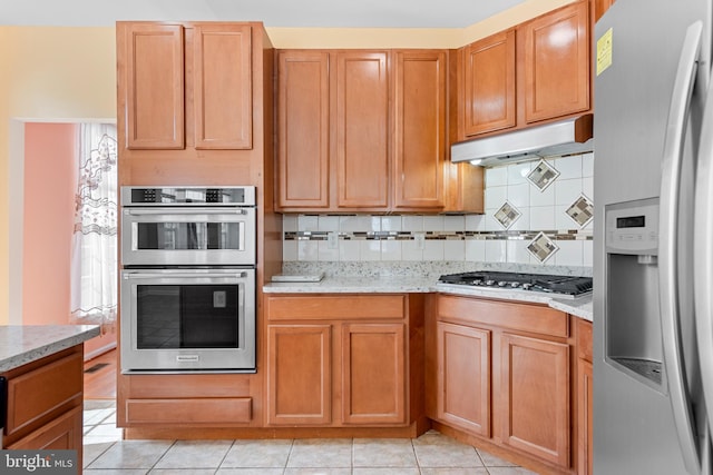 kitchen with decorative backsplash, light stone countertops, stainless steel appliances, and light tile patterned floors