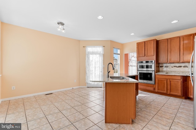 kitchen with a center island with sink, a breakfast bar area, light tile patterned floors, sink, and stainless steel double oven