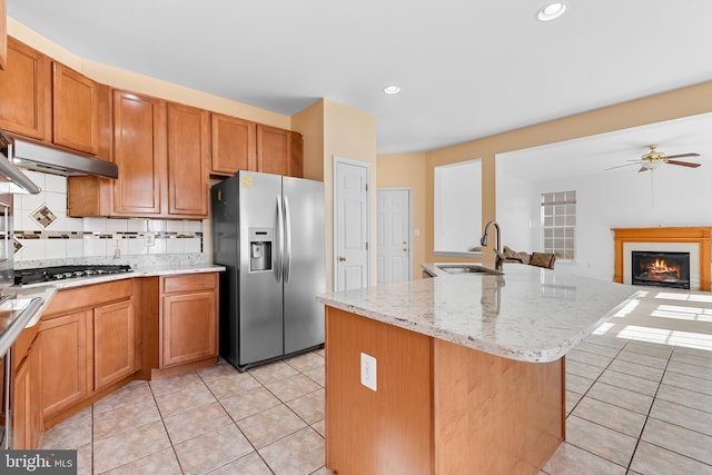 kitchen featuring an island with sink, stainless steel appliances, backsplash, sink, and light stone countertops