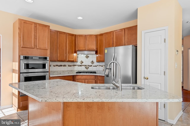 kitchen featuring light stone counters, stainless steel appliances, and a center island with sink