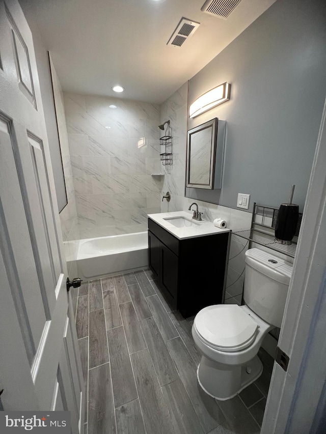 full bathroom featuring toilet, vanity, tiled shower / bath, and tile walls