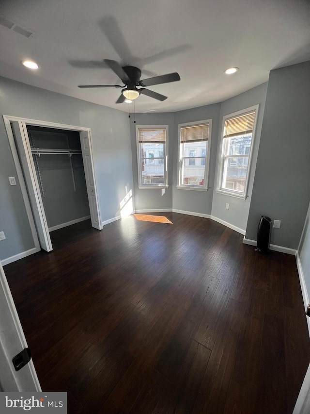 unfurnished bedroom with dark hardwood / wood-style flooring, a closet, multiple windows, and ceiling fan