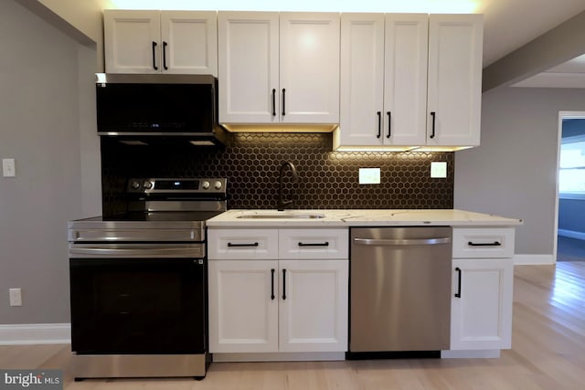 kitchen with white cabinets, appliances with stainless steel finishes, light stone countertops, light hardwood / wood-style flooring, and sink