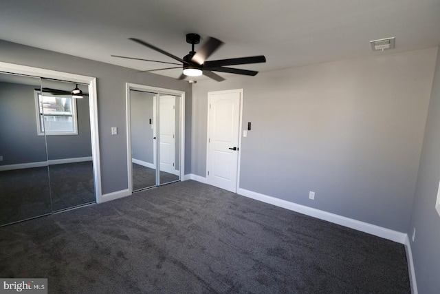 unfurnished bedroom featuring ceiling fan, two closets, and dark carpet