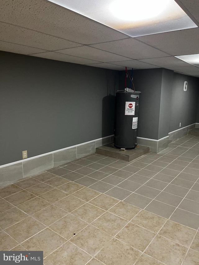 basement featuring a paneled ceiling, tile patterned floors, and water heater