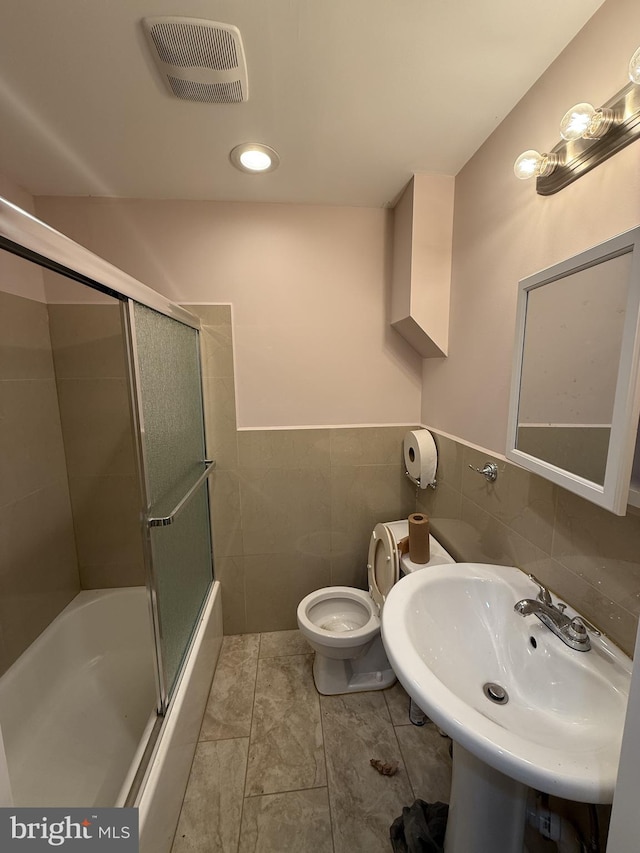 full bathroom with sink, shower / bath combination with glass door, toilet, tile patterned floors, and tile walls