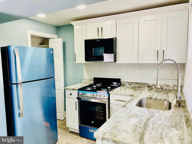 kitchen with backsplash, sink, white cabinetry, appliances with stainless steel finishes, and light stone counters