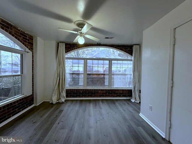 empty room featuring ceiling fan, wood-type flooring, and brick wall