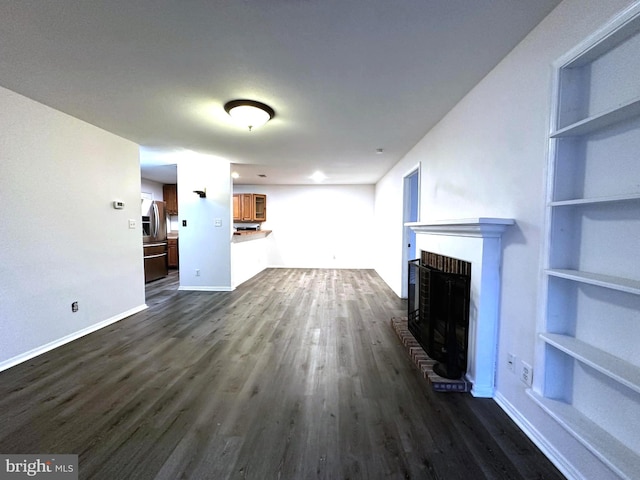 unfurnished living room featuring built in shelves, a brick fireplace, and dark wood-type flooring