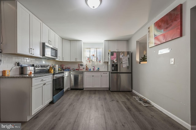 kitchen featuring appliances with stainless steel finishes, white cabinets, hardwood / wood-style flooring, dark stone countertops, and decorative backsplash