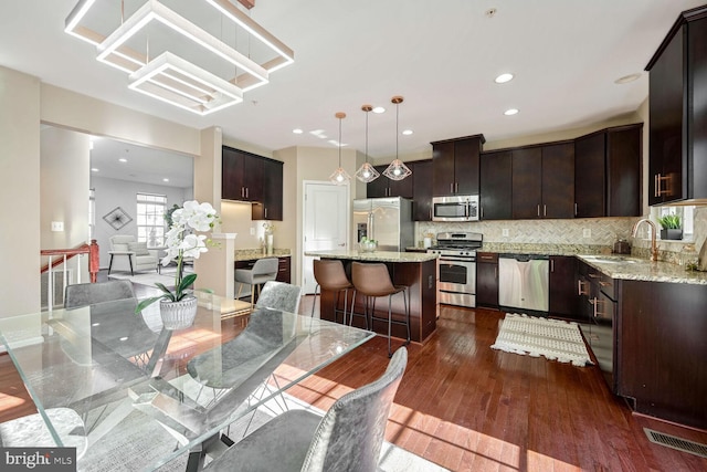 kitchen featuring sink, dark hardwood / wood-style floors, decorative light fixtures, a kitchen island, and appliances with stainless steel finishes