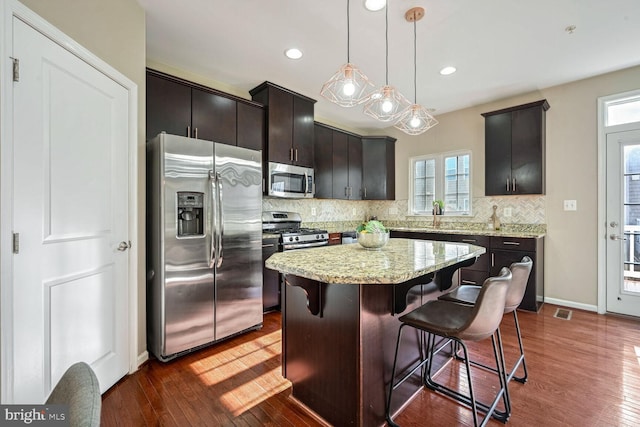 kitchen featuring dark wood-type flooring, a kitchen breakfast bar, decorative backsplash, a kitchen island, and appliances with stainless steel finishes