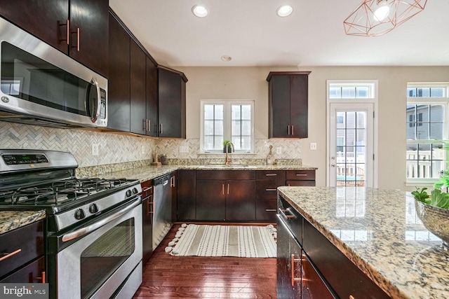 kitchen with light stone countertops, appliances with stainless steel finishes, dark brown cabinetry, dark wood-type flooring, and sink