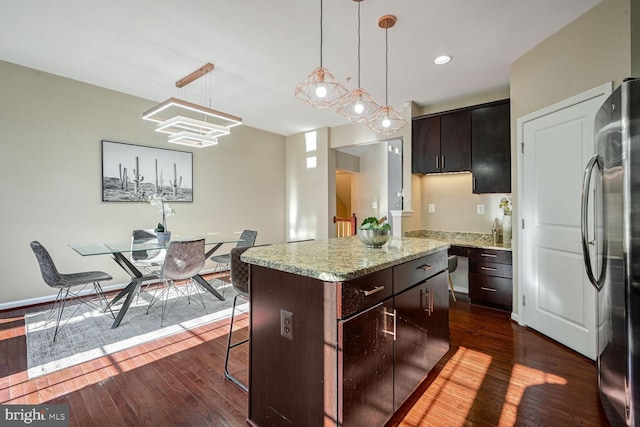 kitchen featuring stainless steel fridge, dark brown cabinetry, dark hardwood / wood-style floors, a kitchen island, and hanging light fixtures