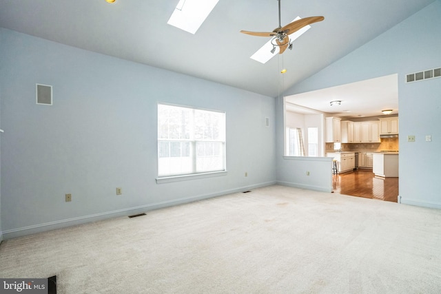 unfurnished living room featuring ceiling fan, a skylight, light colored carpet, and high vaulted ceiling