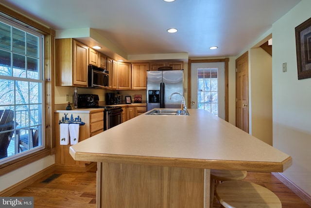 kitchen with an island with sink, black / electric stove, light hardwood / wood-style floors, stainless steel refrigerator with ice dispenser, and sink