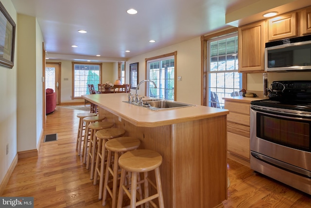 kitchen with light hardwood / wood-style flooring, sink, stainless steel appliances, a breakfast bar, and a center island with sink