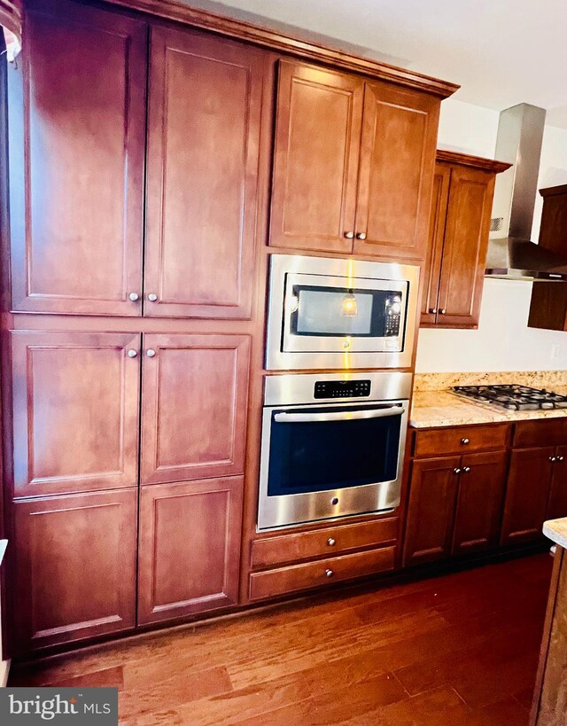 kitchen featuring light stone countertops, dark hardwood / wood-style flooring, wall chimney range hood, and appliances with stainless steel finishes