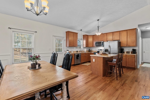 kitchen with hanging light fixtures, appliances with stainless steel finishes, light wood-type flooring, vaulted ceiling, and a center island