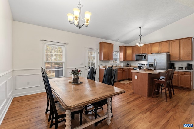 dining room with an inviting chandelier, lofted ceiling, sink, and light wood-type flooring