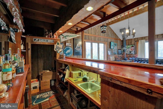 bar with a notable chandelier, lofted ceiling with beams, sink, and wooden walls