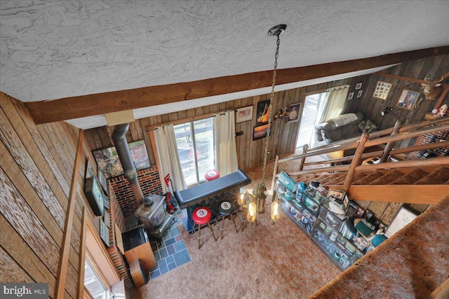 living room with wooden walls, lofted ceiling with beams, a textured ceiling, and a wood stove