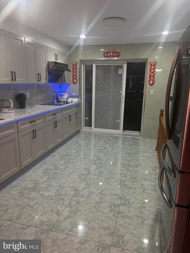 kitchen with gray cabinets, stainless steel fridge, black stovetop, and tasteful backsplash