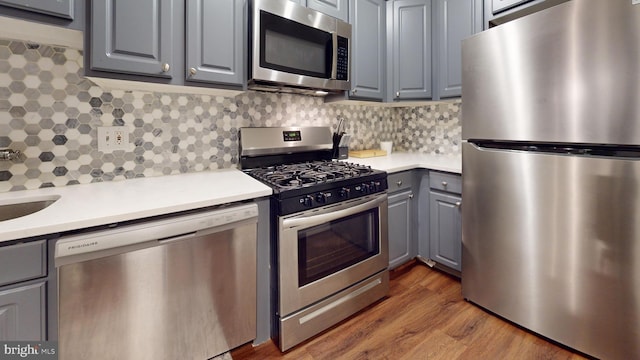 kitchen with gray cabinets, tasteful backsplash, appliances with stainless steel finishes, and hardwood / wood-style flooring